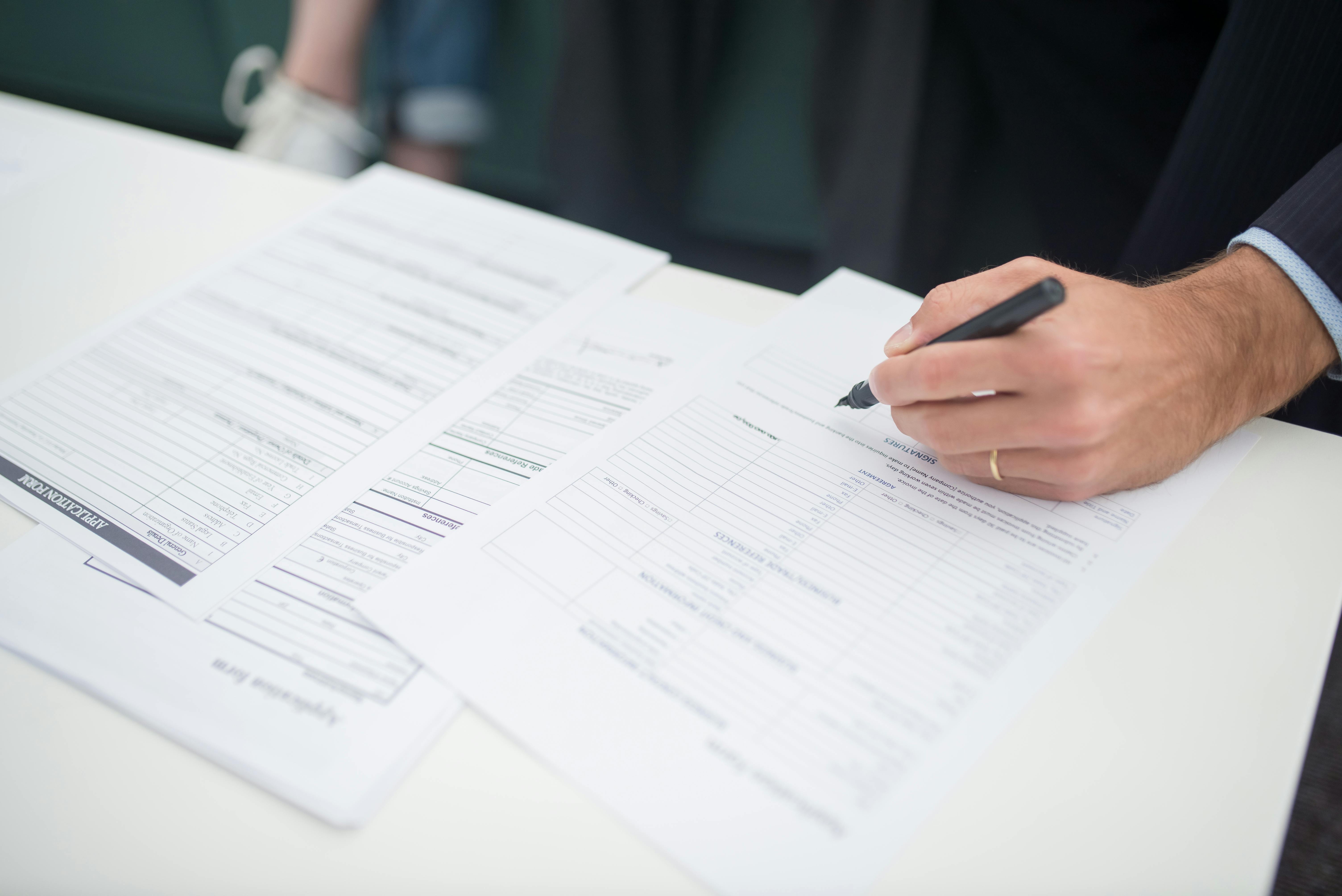 Hand with Pen on Documents on Desk
